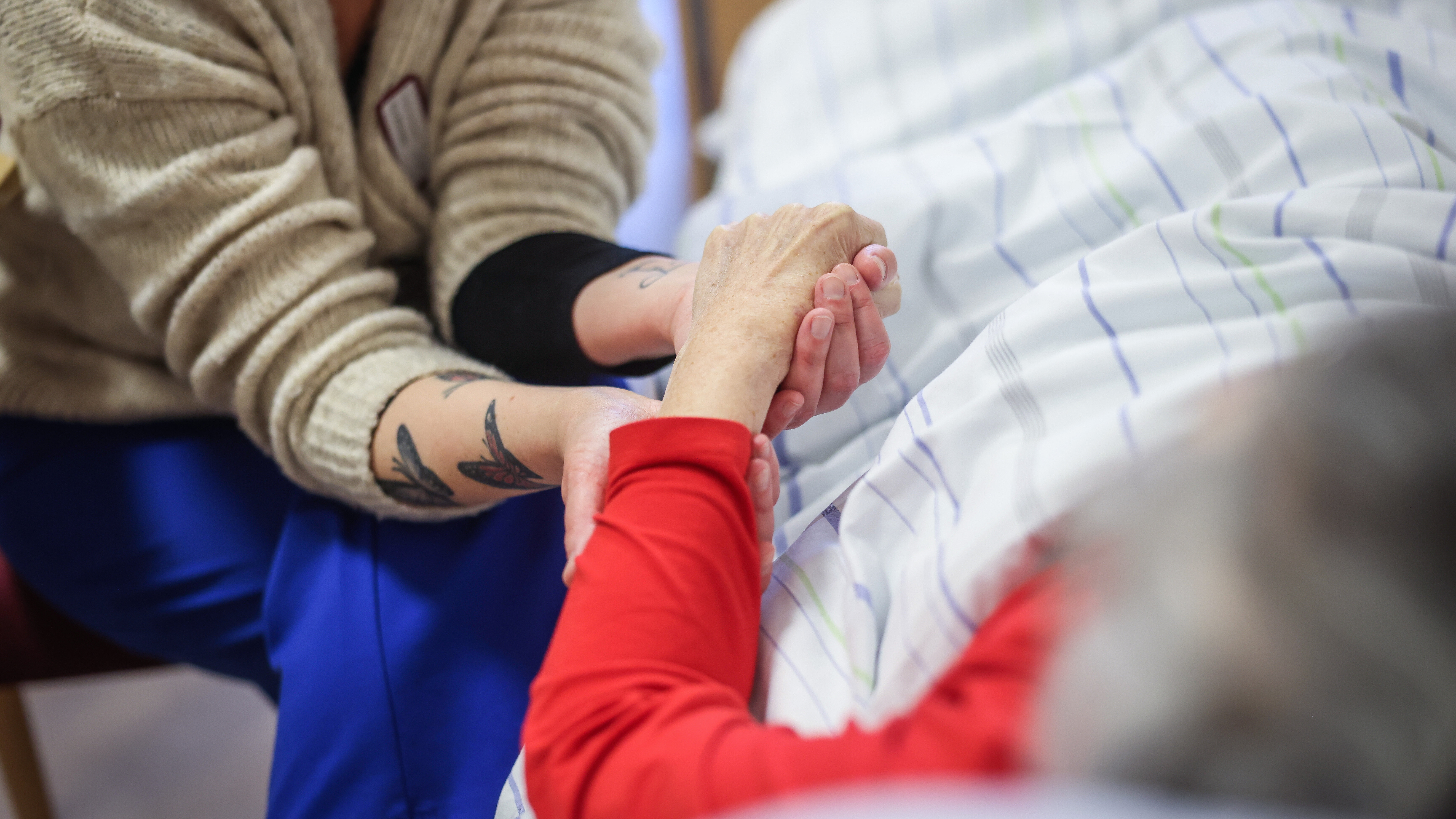 Mitarbeiterin sitzt neben dem Bett einer älteren Frau und hält Ihre Hand.