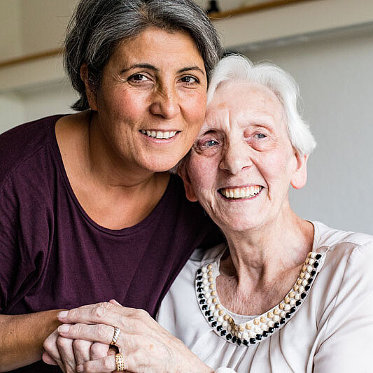 Eine ältere Dame lächelt hält die Hand einer Mitarbeiterin.