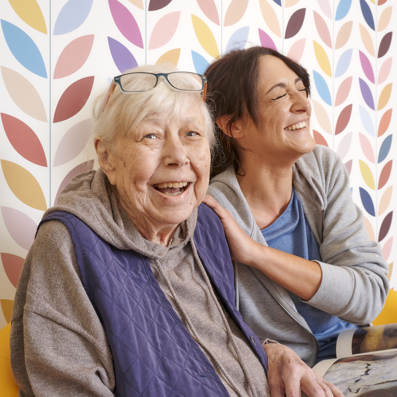 Seniorin und junge Frau sitzen nebeneinander und haben Spaß
