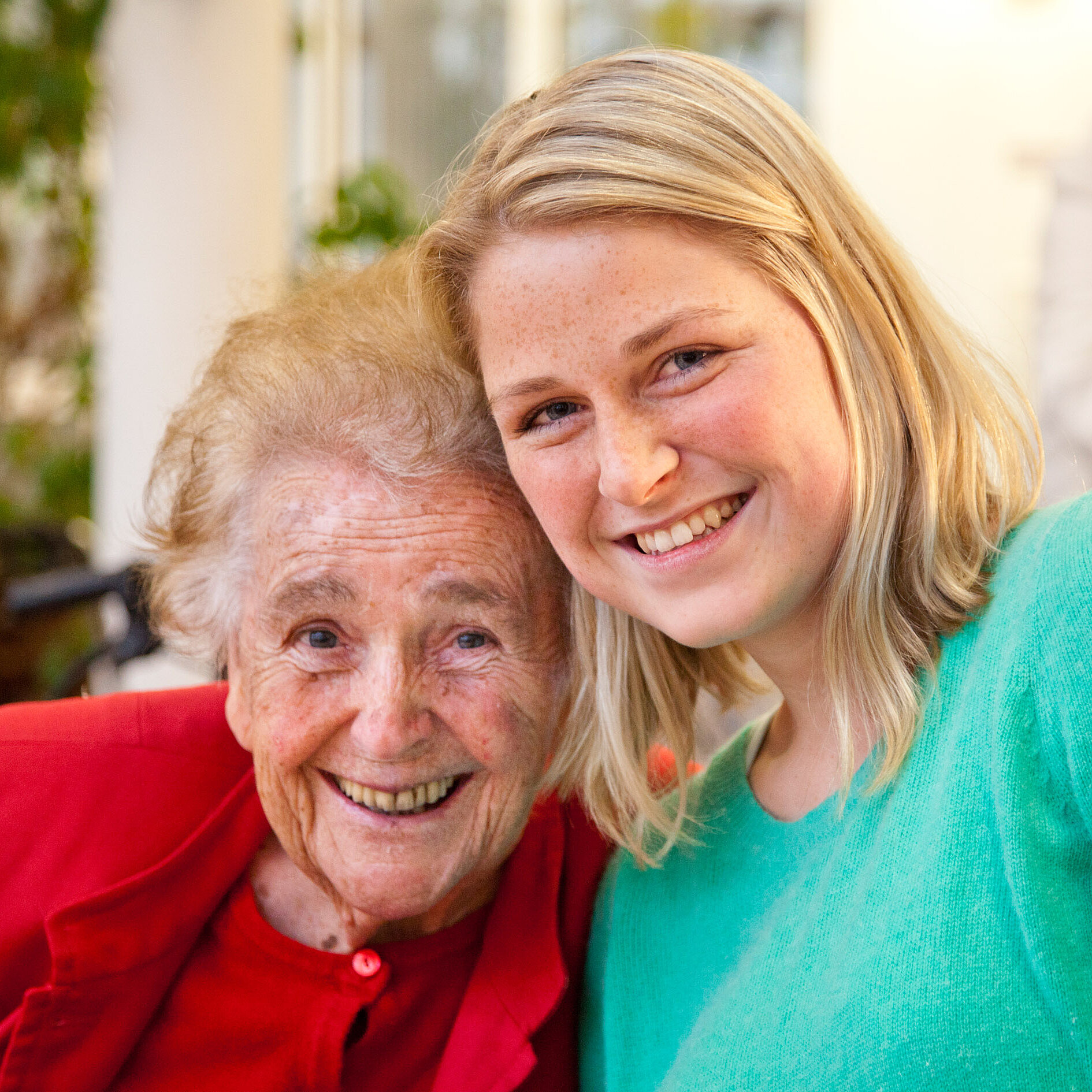 Seniorin und junge Frau sitzen nebeneinander und lächeln